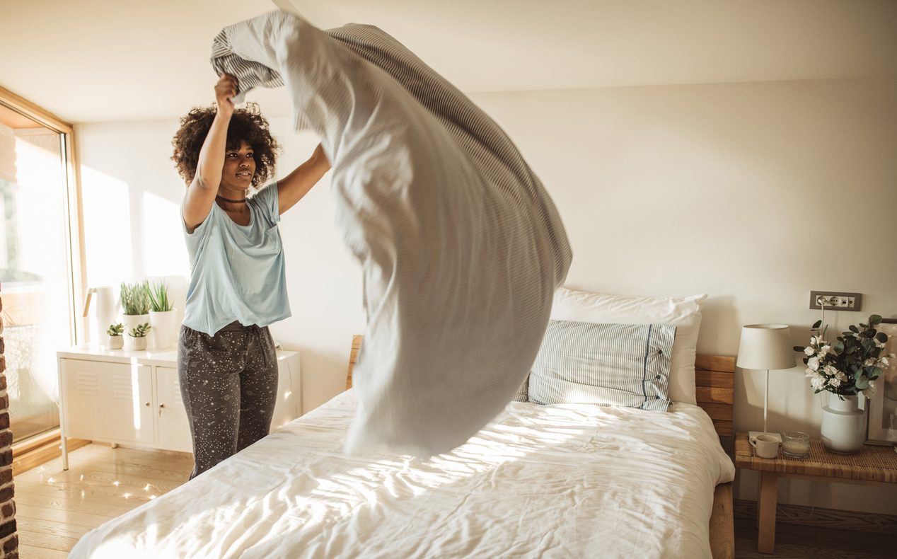 Young woman making bed at home. She is in pajamas. Doing her morning routine.